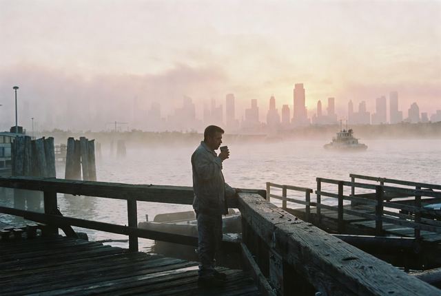 5:30 AM • Red Hook, Brooklyn — Harbor's First Light: Lone dockworker sips coffee on a weathered pier as mist rises from the water. Manhattan skyline silhouette in soft pink.
