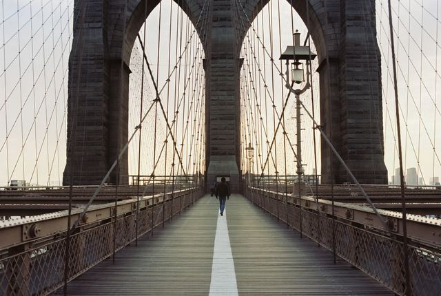 9:05 AM • Brooklyn Bridge — Bridge Crossing: Early commuter walks the pedestrian path. Dramatic cables and stone towers frame the sparkling East River below.