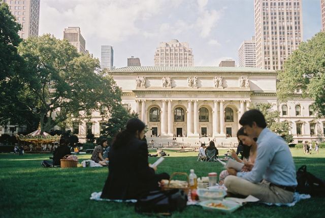 12:15 PM • Bryant Park, Midtown — Library Lawn Picnic: Office workers and readers spread blankets on the green lawn in front of the grand NYPL building.